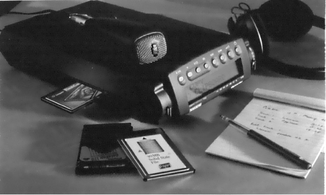 Photograph of a Digicorder with microphone and headphones lying on a desk with a notepad in front of it