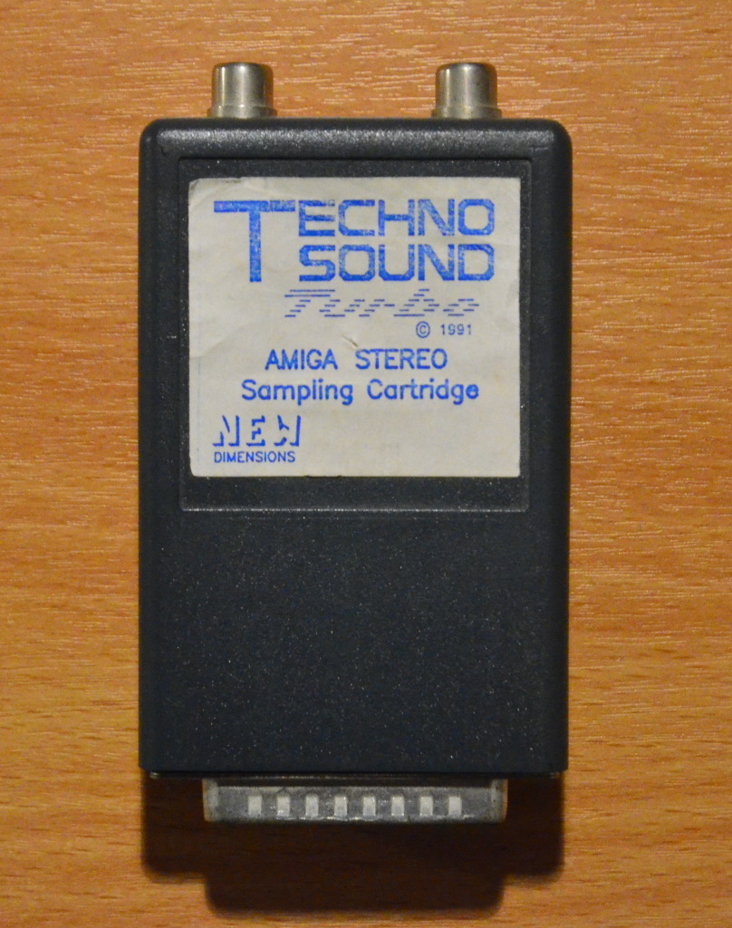 Showing the sampler hardware, which is a grey box with a white label reading "TechnoSound Turbo 1991", "Amiga stereo sampling cartridge" and "New Dimensions"